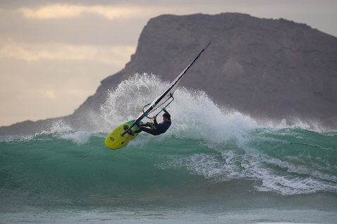 Duotone Grip [Quad] D/LAB windsurf board while wave riding at the ocean beach with rocky headland