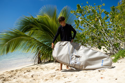 Duotone Wing Boardbag Single in hellgrau beim Transport am Strand mit Palmen
