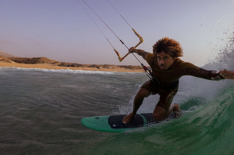 Duotone Whip SLS wave kiteboard during kitesurfing at ocean beach with desert dunes