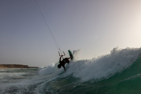 Duotone Whip SLS wave kiteboard during kitesurfing on ocean beach with rocky coastline