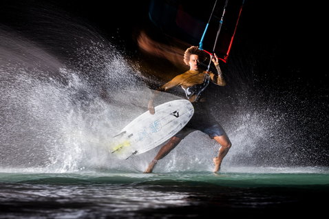 Duotone Whip D/LAB wave kiteboard durante el surf de olas en el océano de noche