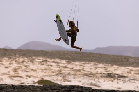 Duotone Whip D/LAB kite surfboard durante kitesurf en una playa costera árida con dunas de arena y montañas