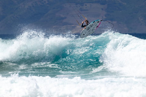 Duotone Volt D/LAB kite surfboard lors du surf de vagues sur plage océanique avec montagne en arrière-plan