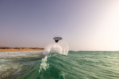 Duotone Volt D/LAB kite surfboard lors du surf de vagues sur une plage océanique avec littoral désertique