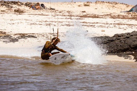 Duotone Volt D/LAB wave kiteboard lors du kitesurf sur une plage peu profonde avec zones sableuses et rochers