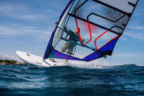 Duotone Blitz D/LAB windsurf board during windsurfing on open ocean with rocky coastline in background