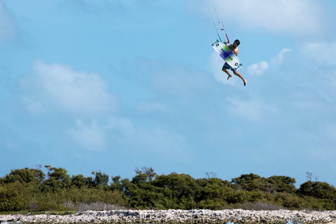 Duotone Select SLS Twin-Tip-Kiteboard beim Kitesurfen an einem Küstenstrand mit niedrigem Bewuchs