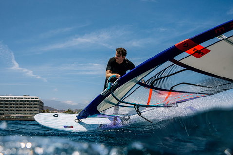 Duotone Falcon Fin SLS planche de windsurf lors de windsurf dans une baie océanique avec ville côtière