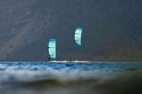 Duotone Rebel D/LAB LEI kite durante il kitesurf su un lago di montagna con colline boscose