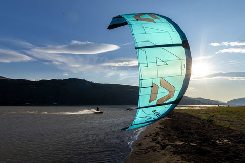 Duotone Rebel D/LAB LEI kite durante il kitesurf su una spiaggia lacustre con montagne