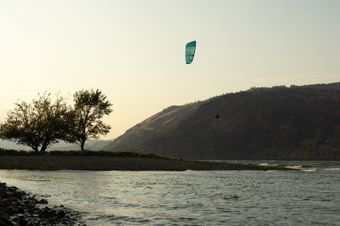 Duotone Rebel D/LAB LEI kite durante il kitesurf in una gola fluviale con colline e alberi
