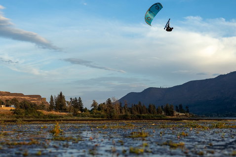 Duotone Rebel D/LAB LEI kite durante il kitesurf su acque piatte di fiume interno con montagne