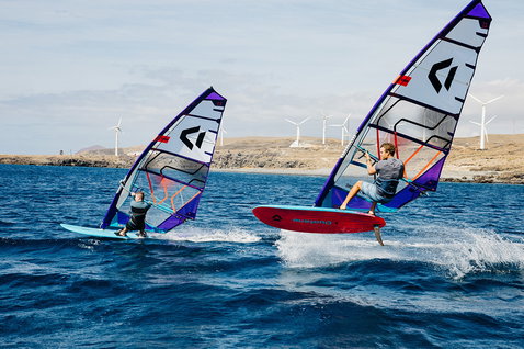 Duotone S_Pace Freeride Windsurf-Segel beim Freeriden an einer felsigen Küste mit Windrädern im Hintergrund