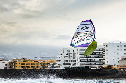 Duotone freeride sail while foiling at a coastal urban waterfront with breaking waves