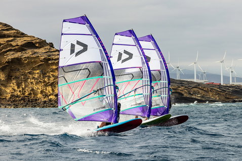 Freeride sail during windsurfing on the ocean with a rocky coastline and wind turbines