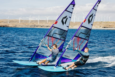 Planche de windsurf Duotone Blitz SB lors du windsurf sur la côte océanique avec paysage aride et éoliennes en arrière-plan