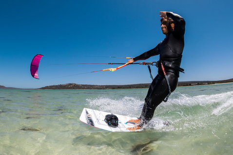 Kiteboard twin-tip lors du kitesurf dans un lagon océanique peu profond avec plage de sable et collines en arrière-plan