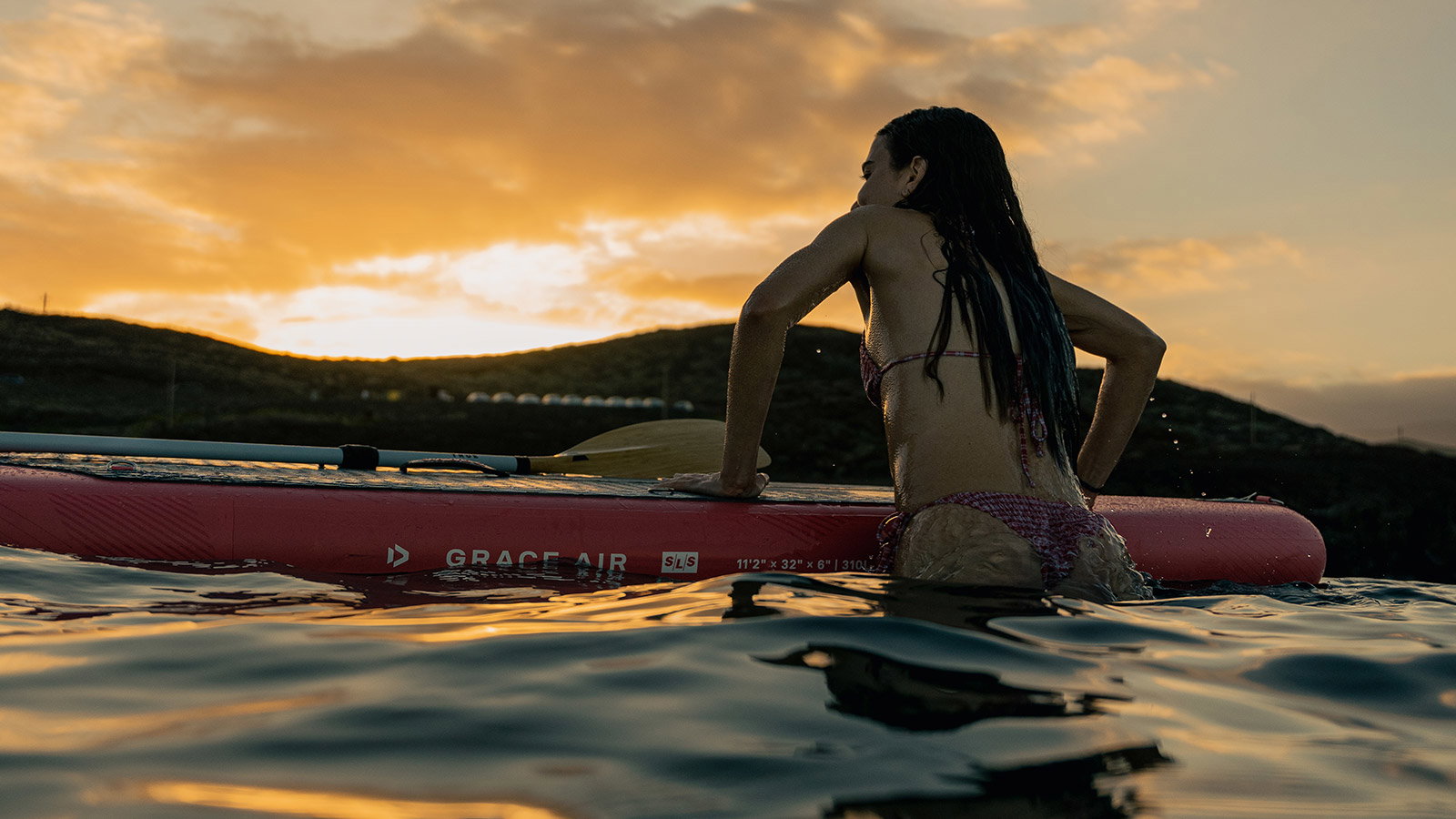 Duotone Grace Air SLS inflatable SUP board 11'2" in coral during stand-up paddling at golden-hour sunset