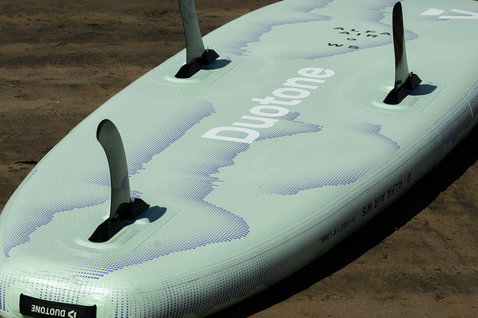 Tavola SUP gonfiabile Duotone Alfa WS Air con pinna thruster in verde salvia sulla sabbia
