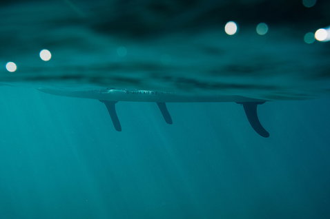 Duotone Alfa WS Air aufblasbares Windsurf-SUP-Board Unterwasseransicht mit Drei-Finnen-Setup im tiefen türkisen Wasser