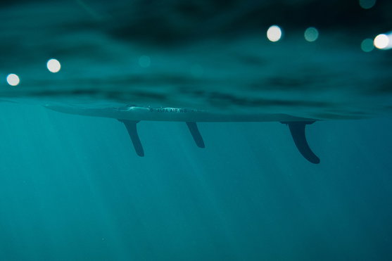 Duotone Alfa WS Air inflatable windsurf SUP board underwater side view showing three-fin setup in deep teal ocean water