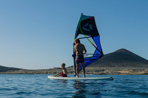 Duotone Alfa WS Air iSUP Windsurf-Paket beim Windsurfen auf ruhigem Wasser vor vulkanischer Küstenlandschaft