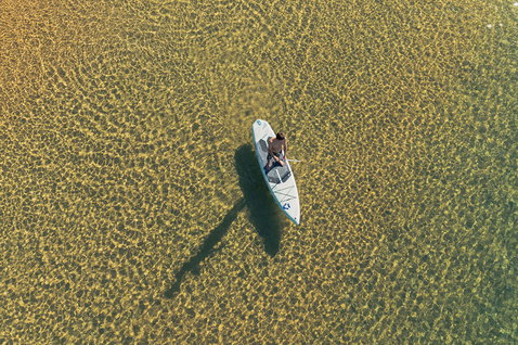 Duotone Blitz Air SLS inflatable SUP board during touring paddling, aerial view over clear water