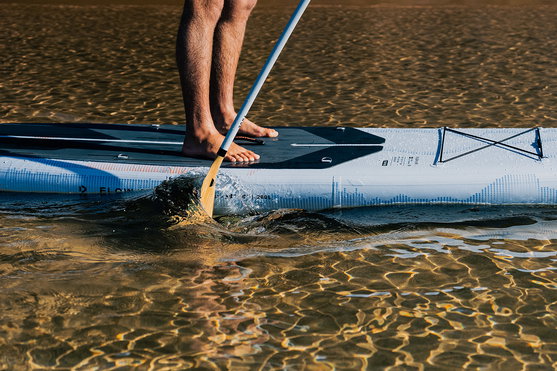 Duotone Flow Air SLS inflatable SUP board during stand up paddling in shallow golden water at sunset