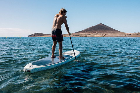 Tavola SUP gonfiabile Duotone Alfa WS Air durante il paddling in una baia costiera con vulcano sullo sfondo