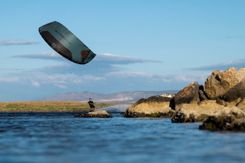 Duotone Evo SLS Porsche Edition LEI kite during kitesurfing at a rocky coastal lagoon in dark teal