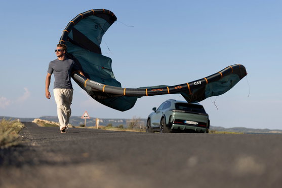 Duotone Evo SLS LEI Kite in dunkelgrün und orange beim Transport an der Küste mit Porsche im Hintergrund