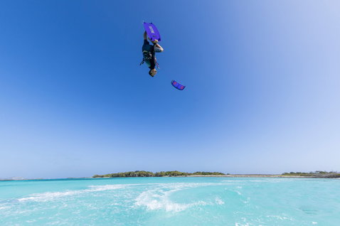 Duotone Dice SLS LEI kite during freestyle kitesurfing above a tropical turquoise lagoon in blue and purple
