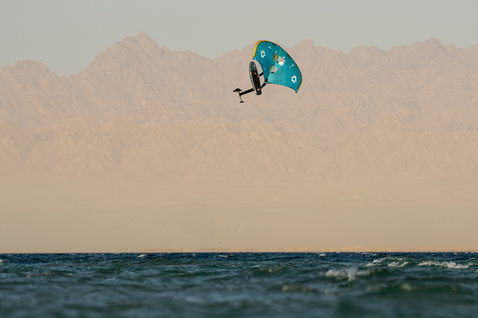Duotone Unit D/LAB foil wing durante il wing foiling sull'oceano con sfondo montuoso