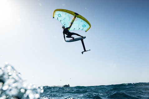 Duotone Unit D/LAB foil wing durante il wing foiling sopra il mare in teal e giallo