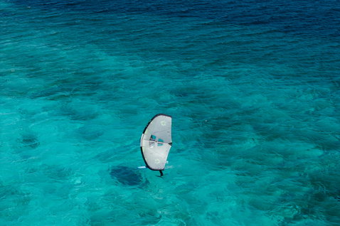 Duotone Unit Foilwing beim Wing Foiling über türkisfarbenem Riff aus der Vogelperspektive