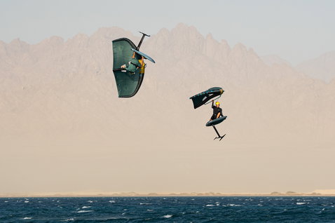 Duotone Unit SLS Foilwing beim Wing Foiling mit zwei Athleten in der Luft über dem Meer vor Bergkulisse