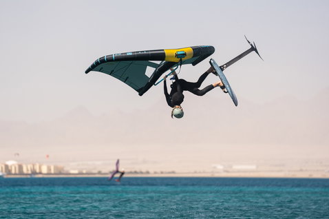 Duotone Unit SLS Foilwing beim Wing Foiling mit Aerial-Trick über dem Meer in dunklem Petrol und Gelb