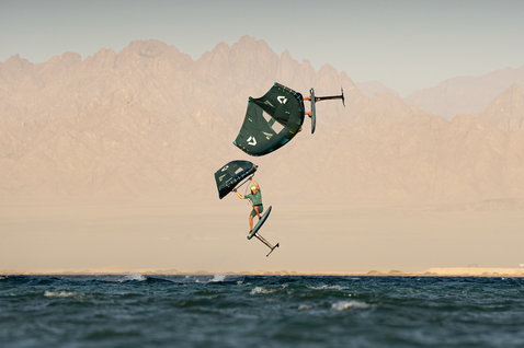 Duotone Unit SLS Wing Foil mit Sky Style Foilboard beim Wing Foiling über dem Meer mit Bergkulisse
