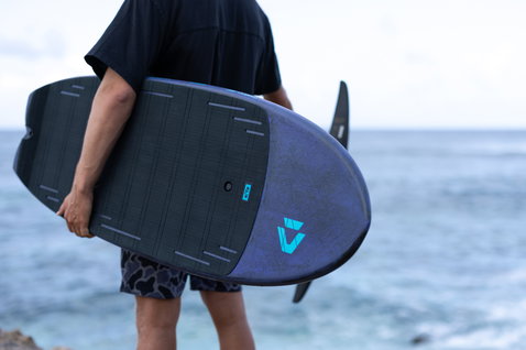 Duotone Crush SLS prone foil board held by athlete at coastal shoreline in dark navy