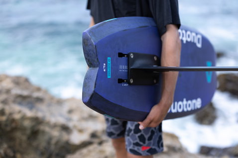 Duotone Crush SLS prone foil board in dark navy during prone foiling at a rocky coastline