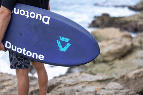 Duotone Crush SLS prone foil board in deep navy blue during prone foiling at rocky coastline