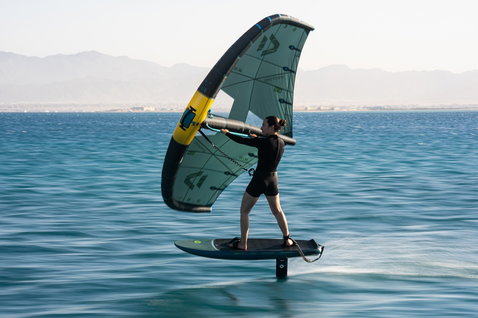 Planche de foil Duotone Skybrid SLS en wing foiling sur eau plate avec montagnes en arrière-plan