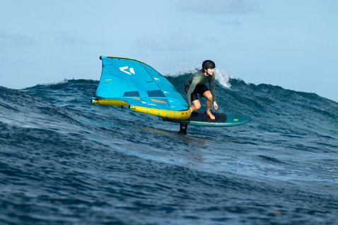 Planche de foil Duotone Skybrid SLS lors de wing foiling sur vagues océaniques en bleu pétrole et jaune