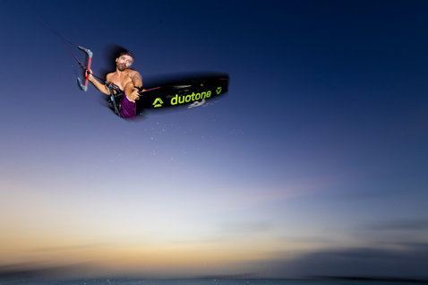 Tabla de kitesurf twin-tip Duotone Select SLS durante un salto aéreo al atardecer sobre el mar