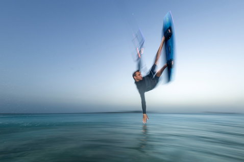 Tabla de kitesurf twin-tip Duotone Select SLS freeride en azul acero sostenida por un rider en el océano al atardecer
