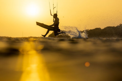 Tabla de kitesurf twin-tip Duotone Select SLS durante una sesión de kitesurf en la hora dorada sobre el océano