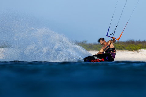 Tabla de kitesurf twin-tip Duotone Select Concept Blue durante una sesión de kitesurf en playa tropical