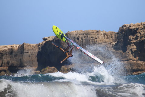 Duotone Cosmic D/LAB wave windsurf board during wave riding at rocky coastal cliffs in neon yellow-green