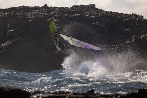 Duotone Cosmic D/LAB wave windsurf board during wave riding at a volcanic rocky coastline