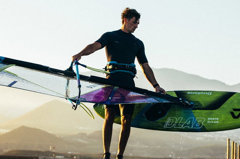 Duotone Skate D/LAB freestyle windsurf board carried at the coast during golden-hour light